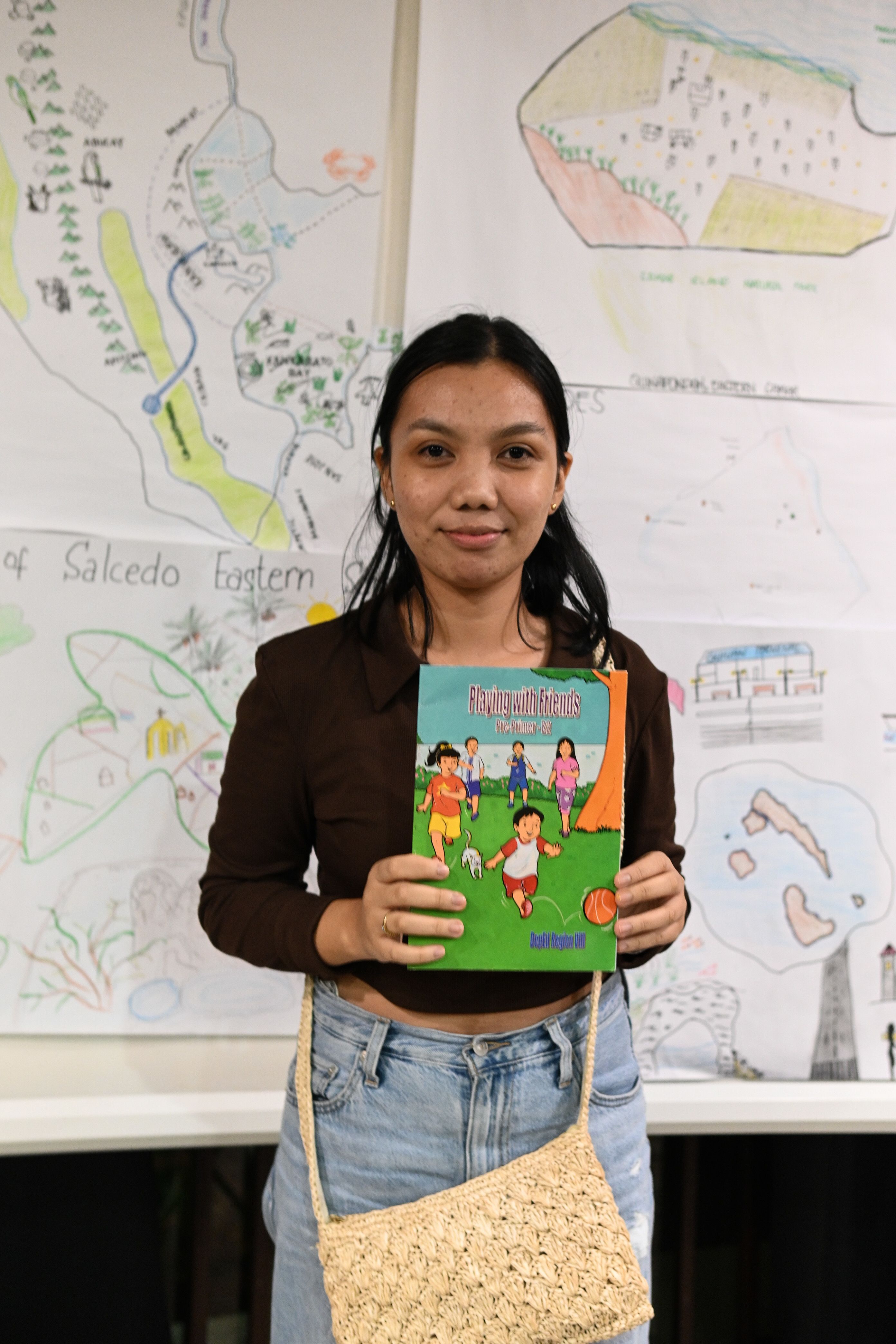A photo of Queenee dela Cruz standing in a classroom, holding her object of memory: a kintergarten book