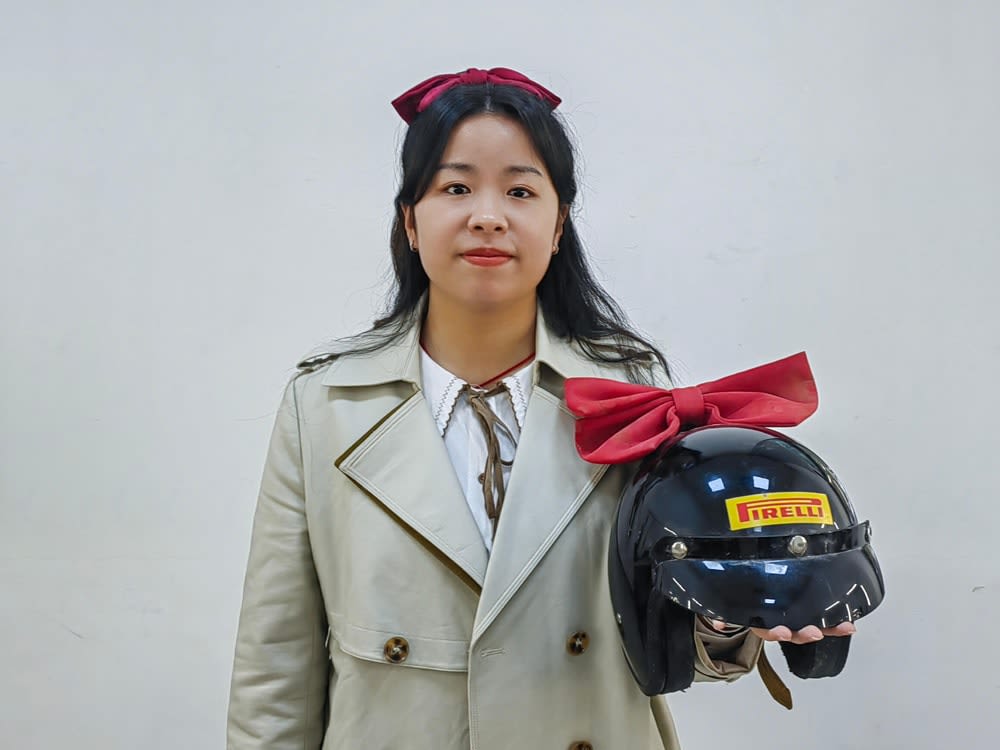 A portrait of Wu Puhui's holding her object of memory: a bike helmet with a red ribbon