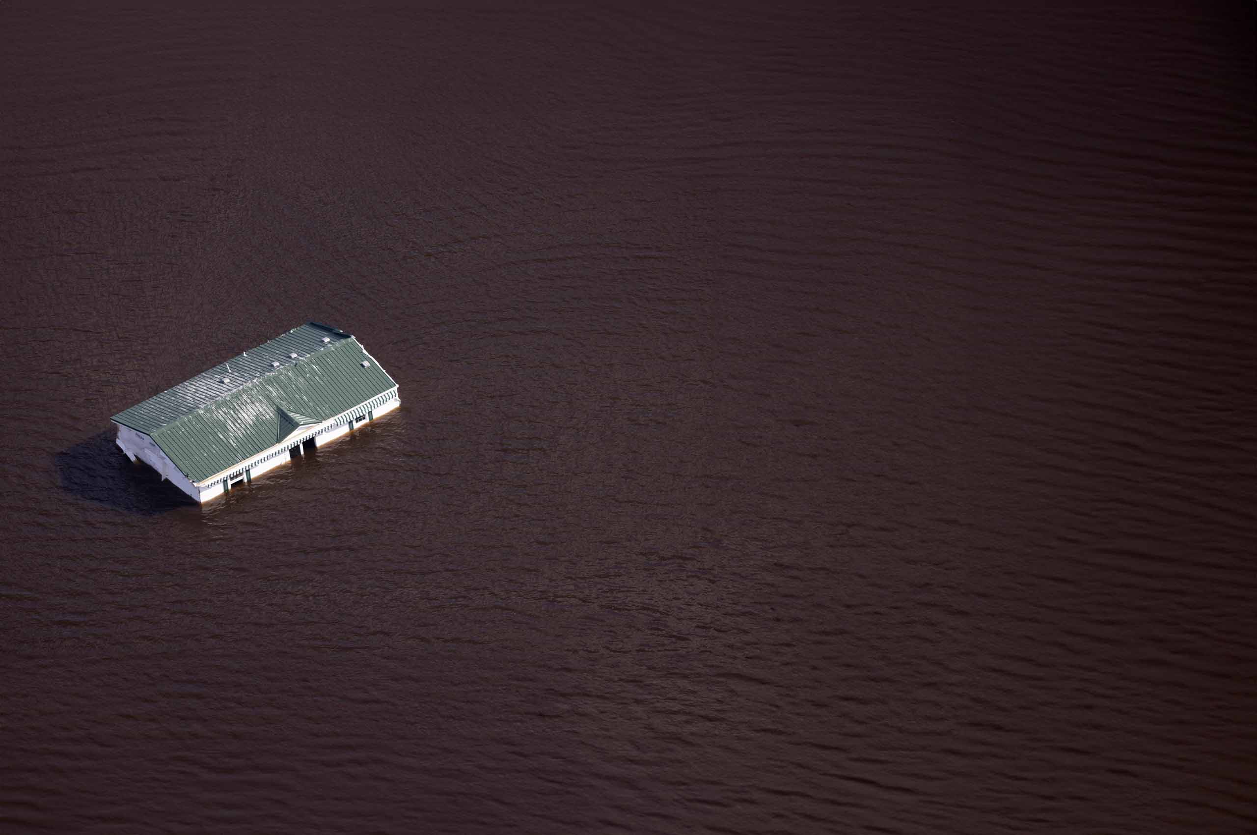 an aerial photo of house almost totally submerged under flooded water